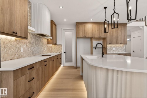 Kitchen with light stone counters, wood finish cabinetry, hanging light fixtures, light wood-style flooring, and backsplash - 9 Elwyck Gate, Spruce Grove, AB - Indoor Photo Showing Kitchen With Upgraded Kitchen