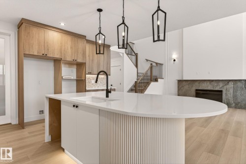 Kitchen with modern cabinets, light wood-type flooring, light stone counters, pendant lighting, and a kitchen island with sink - 9 Elwyck Gate, Spruce Grove, AB - Indoor