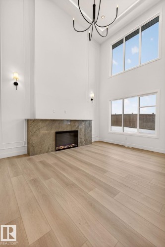 Unfurnished living room featuring a high ceiling, a high end fireplace, light wood finished floors, and hanging lights - 9 Elwyck Gate, Spruce Grove, AB - Indoor Photo Showing Other Room With Fireplace