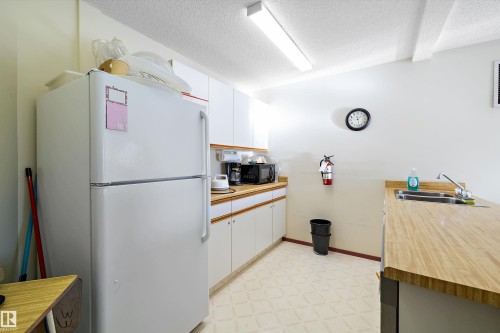Kitchen featuring freestanding refrigerator, white cabinets, light flooring, a textured ceiling, and light countertops - 218 18012 95 Avenue, Edmonton, AB - Indoor Photo Showing Kitchen With Double Sink