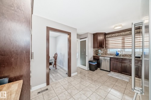 Kitchen with dark wood finish cabinets, light tile patterned floors, stainless steel appliances, decorative backsplash, and light stone countertops - 12203 147 Avenue, Edmonton, AB - Indoor