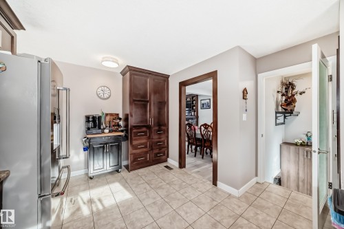 Kitchen with stainless steel fridge with ice dispenser, dark wood finish cabinetry, and light tile patterned floors - 12203 147 Avenue, Edmonton, AB - Indoor