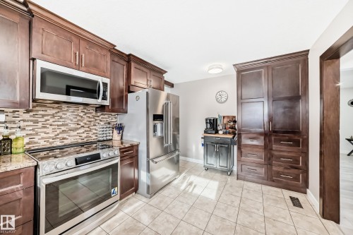 Kitchen with stainless steel appliances, dark wood finish cabinets, light tile patterned floors, and light stone counters - 12203 147 Avenue, Edmonton, AB - Indoor Photo Showing Kitchen With Stainless Steel Kitchen With Upgraded Kitchen