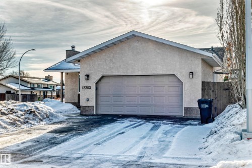 View of snowy exterior featuring stucco siding, a chimney, a garage, and driveway - 12203 147 Avenue, Edmonton, AB - Outdoor