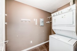 Laundry room featuring electric panel, stacked washer and clothes dryer, and dark tile patterned flooring - 