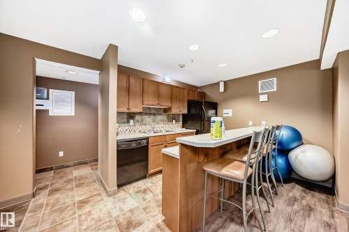 Kitchen with a peninsula, light countertops, a breakfast bar area, wood finish cabinets, and black appliances - 125 278 Suder Greens Drive, Edmonton, AB - Indoor Photo Showing Kitchen