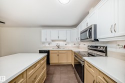 Kitchen with stainless steel appliances, dark tile patterned floors, light wood finish cabinets, and light stone countertops - 