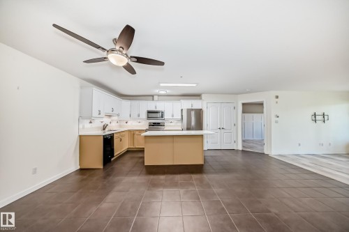 Two tone kitchen with light countertops, stainless steel appliances, a center island, open floor plan, and dark tile patterned floors - 125 278 Suder Greens Drive, Edmonton, AB - Indoor Photo Showing Kitchen