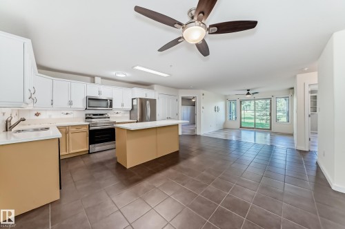 Kitchen featuring stainless steel appliances, a kitchen island, a ceiling fan, dark tile patterned flooring, and open floor plan - 125 278 Suder Greens Drive, Edmonton, AB - Indoor Photo Showing Kitchen