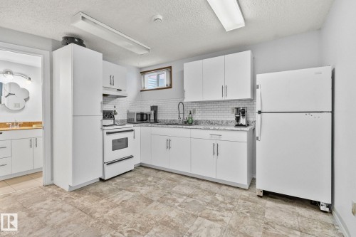 Kitchen featuring white appliances, white cabinets, under cabinet range hood, decorative backsplash, and a textured ceiling - 17523 95 Street, Edmonton, AB - Indoor Photo Showing Kitchen