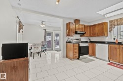Kitchen with brown cabinetry, stainless steel electric range oven, white dishwasher, under cabinet range hood, and a textured ceiling - 