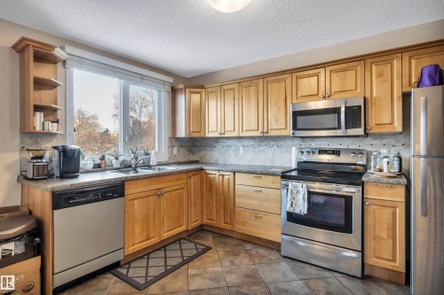 Kitchen featuring stainless steel appliances, a textured ceiling, open shelves, backsplash, and dark tile patterned flooring - 402 9929 113 Street, Edmonton, AB - Indoor Photo Showing Kitchen