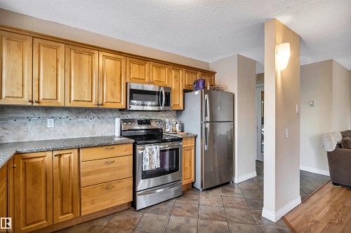 Kitchen with appliances with stainless steel finishes, backsplash, brown cabinets, a textured ceiling, and dark tile patterned flooring - 402 9929 113 Street, Edmonton, AB - Indoor Photo Showing Kitchen