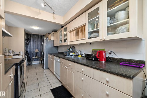 Kitchen with a textured ceiling, stainless steel appliances, glass fronted cabinets, light tile patterned floors, and track lighting - 127 Cornell Court, Edmonton, AB - Indoor Photo Showing Kitchen With Double Sink