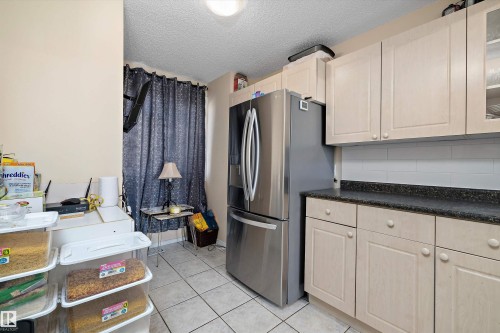 Kitchen with dark countertops, stainless steel fridge with ice dispenser, a textured ceiling, glass insert cabinets, and light tile patterned floors - 127 Cornell Court, Edmonton, AB - Indoor