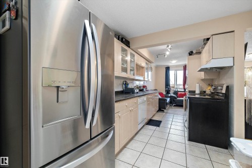 Kitchen featuring stainless steel appliances, glass insert cabinets, light tile patterned floors, decorative backsplash, and a textured ceiling - 127 Cornell Court, Edmonton, AB - Indoor Photo Showing Kitchen
