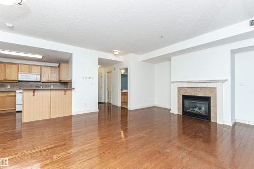 Unfurnished living room featuring a textured ceiling, a fireplace, and dark wood-style flooring - 112 260 Sturgeon Road, St. Albert, AB - Indoor With Fireplace