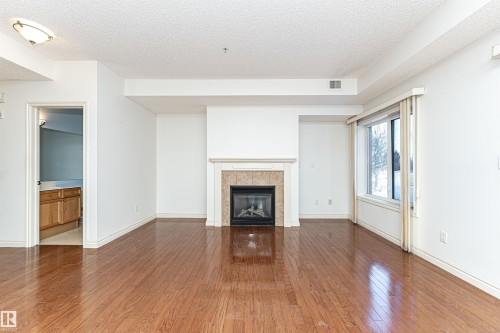 Unfurnished living room with dark wood-style flooring, a textured ceiling, and a tile fireplace - 112 260 Sturgeon Road, St. Albert, AB - Indoor Photo Showing Living Room With Fireplace