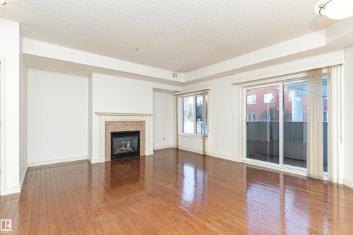 Unfurnished living room with a tile fireplace, wood-type flooring, and a textured ceiling - 112 260 Sturgeon Road, St. Albert, AB - Indoor Photo Showing Living Room With Fireplace