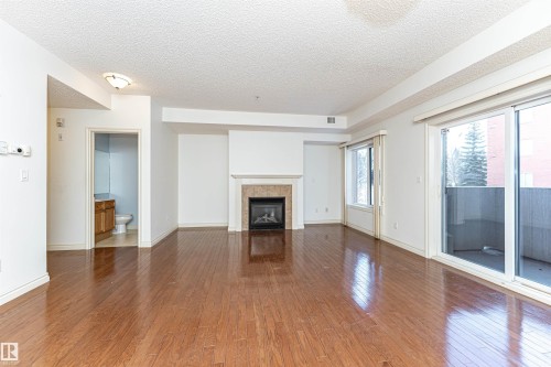 Unfurnished living room featuring dark wood-type flooring, a tiled fireplace, and a textured ceiling - 112 260 Sturgeon Road, St. Albert, AB - Indoor Photo Showing Living Room With Fireplace