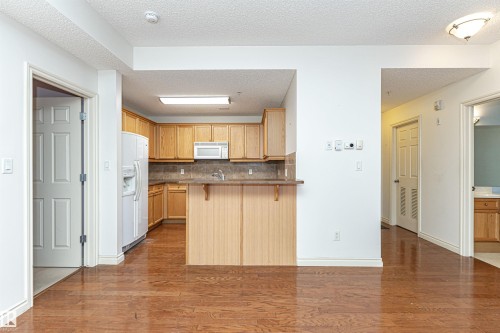 Kitchen with tasteful backsplash, dark wood finished floors, a breakfast bar, a peninsula, and a textured ceiling - 112 260 Sturgeon Road, St. Albert, AB - Indoor Photo Showing Kitchen