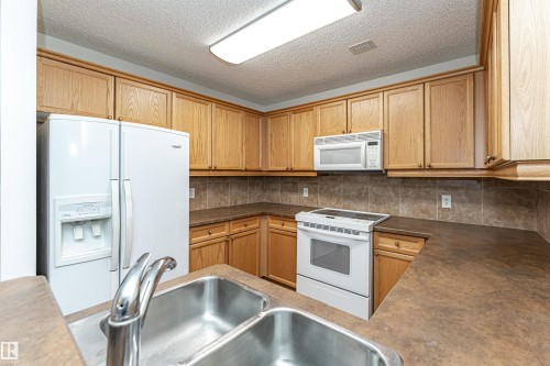 Kitchen featuring white appliances, tasteful backsplash, dark countertops, a textured ceiling, and wood finish cabinets - 112 260 Sturgeon Road, St. Albert, AB - Indoor Photo Showing Kitchen With Double Sink