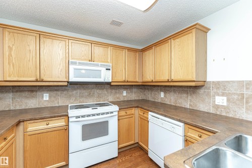Kitchen featuring white appliances, light wood-style floors, light wood finish cabinets, tasteful backsplash, and a textured ceiling - 112 260 Sturgeon Road, St. Albert, AB - Indoor Photo Showing Kitchen With Double Sink