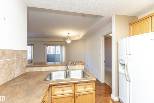 Kitchen featuring a peninsula, white fridge with ice dispenser, a textured ceiling, light wood finish cabinetry, and light countertops - 112 260 Sturgeon Road, St. Albert, AB - Indoor Photo Showing Kitchen With Double Sink