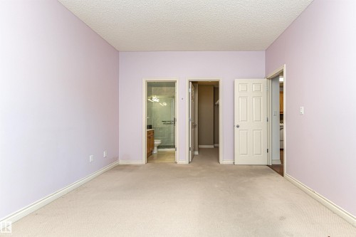 Unfurnished bedroom featuring light colored carpet, a walk in closet, a textured ceiling, and ensuite bath - 112 260 Sturgeon Road, St. Albert, AB - Indoor Photo Showing Other Room