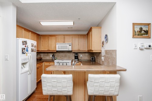 Kitchen featuring a peninsula, white appliances, a breakfast bar area, light countertops, and a textured ceiling - 112 260 Sturgeon Road, St. Albert, AB - Indoor Photo Showing Kitchen