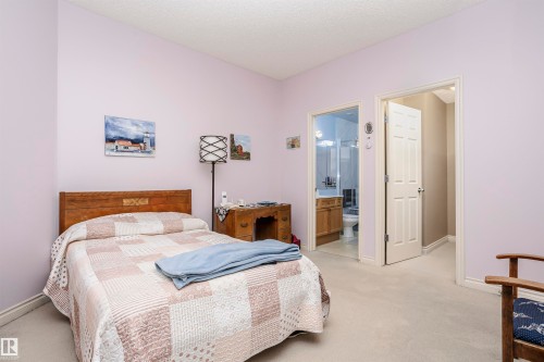 Bedroom with light colored carpet, ensuite bath, and a textured ceiling - 112 260 Sturgeon Road, St. Albert, AB - Indoor Photo Showing Bedroom