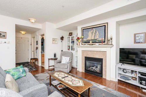 Living area featuring hardwood / wood-style floors, a tiled fireplace, and a textured ceiling - 112 260 Sturgeon Road, St. Albert, AB - Indoor Photo Showing Living Room With Fireplace
