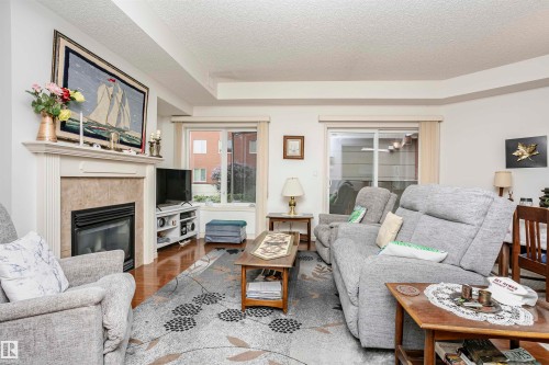 Living room with a glass covered fireplace, wood finished floors, and a textured ceiling - 112 260 Sturgeon Road, St. Albert, AB - Indoor Photo Showing Living Room With Fireplace