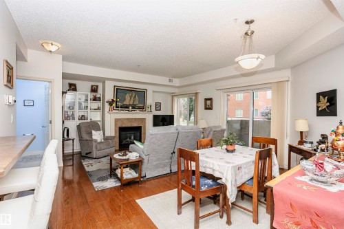 Dining space featuring a glass covered fireplace, a textured ceiling, and hardwood / wood-style flooring - 112 260 Sturgeon Road, St. Albert, AB - Indoor Photo Showing Dining Room With Fireplace
