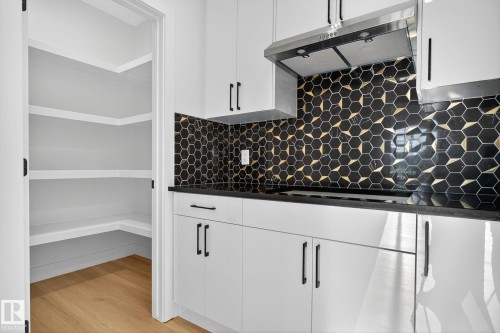 Kitchen with decorative backsplash, white cabinetry, light wood-style flooring, dark stone counters, and black electric stovetop - 3508 6 Street, Edmonton, AB - Indoor