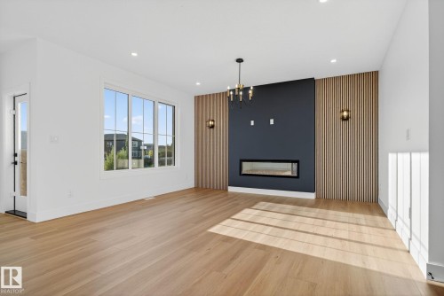 Unfurnished living room with an accent wall, a fireplace, hanging lights, and light wood-type flooring - 3508 6 Street, Edmonton, AB - Indoor Photo Showing Living Room With Fireplace