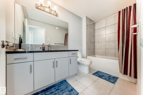 Bathroom with vanity, shower / bathtub combination with curtain, light tile patterned floors, and a textured ceiling - 1002 Stillwater Boulevard, Edmonton, AB - Indoor Photo Showing Bathroom