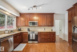 Kitchen featuring stainless steel appliances, light stone countertops, light wood-type flooring, and wood finish cabinets - 