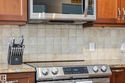 Kitchen with stainless steel appliances, wood finish cabinets, backsplash, and light stone countertops - 