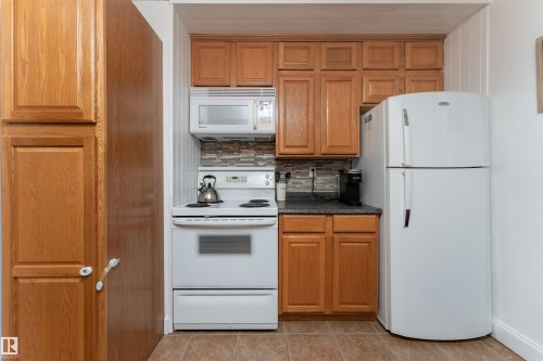 Kitchen with white appliances, decorative backsplash, brown cabinetry, dark countertops, and light tile patterned flooring - 11539 101 Street, Edmonton, AB - Indoor Photo Showing Kitchen