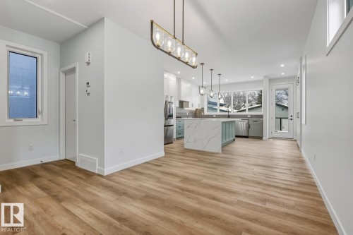 Two tone kitchen with suspended lighting, light wood-type flooring, backsplash, a kitchen island, and stainless steel appliances - 9627 152 Street Nw, Edmonton, AB - Indoor