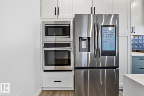 Kitchen featuring stainless steel appliances, light wood finished floors, decorative backsplash, light stone counters, and two tone cabinets - 9627 152 Street Nw, Edmonton, AB - Indoor Photo Showing Kitchen