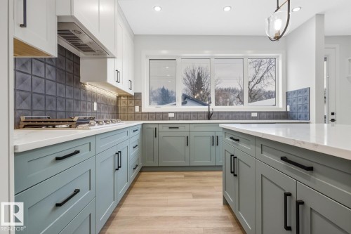 Kitchen with light stone countertops, hanging light fixtures, light wood finished floors, backsplash, and range hood - 9627 152 Street Nw, Edmonton, AB - Indoor Photo Showing Kitchen With Upgraded Kitchen