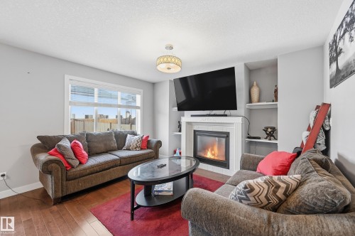 Living area featuring a tiled fireplace, a textured ceiling, and wood-type flooring - 5978 167C Avenue, Edmonton, AB - Indoor Photo Showing Living Room With Fireplace
