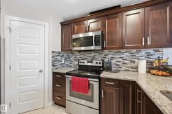Kitchen with stainless steel appliances, dark wood finish cabinetry, light stone countertops, and backsplash - 