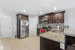 Kitchen with dark wood finish cabinets, stainless steel appliances, a peninsula, light stone counters, and light tile patterned floors - 