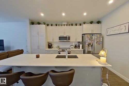 Kitchen with white cabinets, a kitchen breakfast bar, stainless steel appliances, a kitchen island with sink, and backsplash - 4419 Kinsella Green, Edmonton, AB - Indoor Photo Showing Kitchen With Upgraded Kitchen
