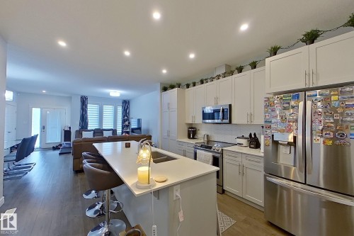Kitchen with stainless steel appliances, white cabinetry, light wood finished floors, decorative backsplash, and open floor plan - 4419 Kinsella Green, Edmonton, AB - Indoor Photo Showing Kitchen With Stainless Steel Kitchen With Upgraded Kitchen