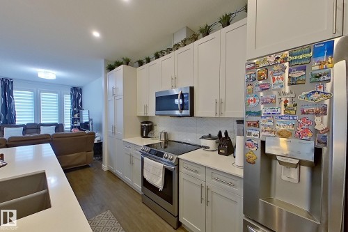 Kitchen with stainless steel appliances, open floor plan, white cabinetry, dark wood-style flooring, and recessed lighting - 4419 Kinsella Green, Edmonton, AB - Indoor Photo Showing Kitchen