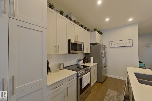 Kitchen featuring stainless steel appliances, recessed lighting, light wood-style flooring, white cabinetry, and backsplash - 4419 Kinsella Green, Edmonton, AB - Indoor Photo Showing Kitchen With Stainless Steel Kitchen With Double Sink